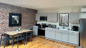 A modern kitchen with a brick wall, a dining table with chairs, and a large window. - Large 2 Bedroom 1 Bath Apartment right on Main Street in Downtown Ellsworth. (Ellsworth)