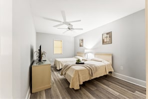 A bedroom with two beds, a ceiling fan, a desk with a computer, and a window with blinds.