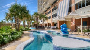 Ein Hotelpoolbereich mit mehreren Pools, Palmen, Liegestühlen und Sonnenschirmen.