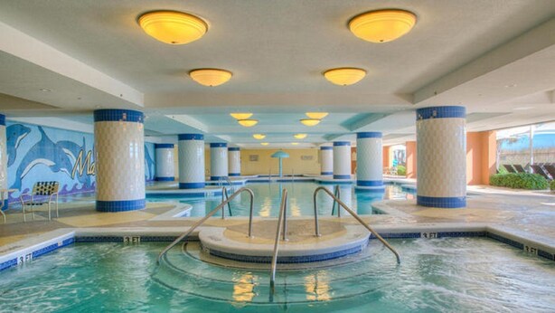 Ein Innenpool mit einem zentralen, runden Whirlpool, umgeben von Säulen und einem Wandgemälde mit Delphinen.