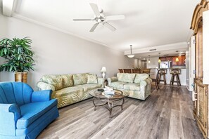 A living room with a blue armchair, two sofas, a coffee table, and a ceiling fan.
