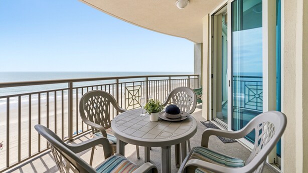 A balcony with a table, chairs, a potted plant, and a decorative hat.
