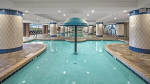 A large indoor swimming pool with a central fountain, surrounded by tiled walls and columns.