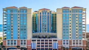 A multi-story hotel with a central atrium, balconies, and a view of the beach.