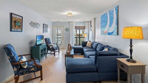 Ein Wohnzimmer mit einem Ecksofa, einem Fernseher und einer Lampe.