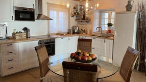 A modern kitchen with white cabinets, a glass dining table, wicker chairs, and a variety of kitchen appliances.