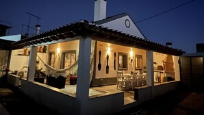 A house with a tiled roof, a chimney, and a dining area with chairs and a table.