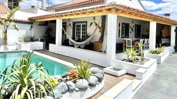 A house with a swimming pool, a hammock, and potted plants.