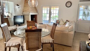 A cozy living room with a fireplace, a round glass table, wicker chairs, a sofa, and a television.