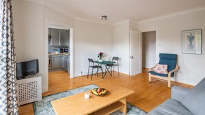 Ein modernes Wohnzimmer mit einer Couch, einem Couchtisch mit Obst, einem Fernseher und einem Essbereich mit Stühlen und einem Tisch.