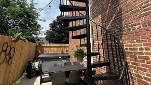 A spiral staircase attached to a brick wall, outdoor seating area with tables and chairs, and a wooden fence. - The Courthouse Loft - History with a hot tub!  (El Paso)