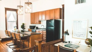 A kitchen with wooden cabinets, a black refrigerator, a dining area with chairs, and a desk with a globe and notebook. - The Courthouse Loft - History with a hot tub!  (El Paso)