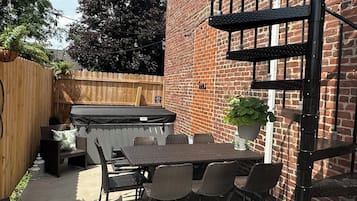 A patio area with a table and chairs, a hot tub, and a brick wall.