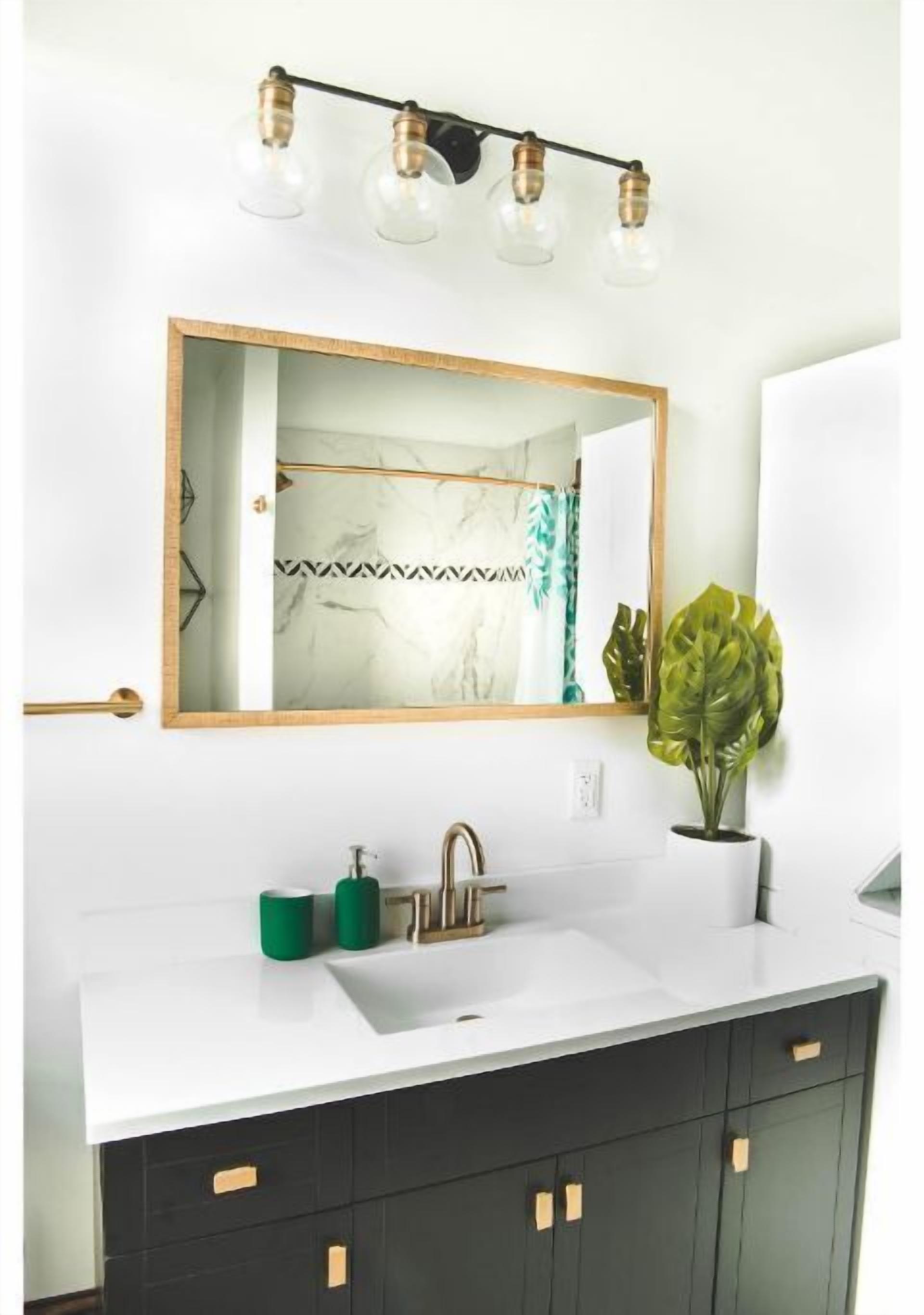 Een badkamer met een wit wastafelmeubel, zwarte kastjes, een spiegel met gouden lijst en een plant.