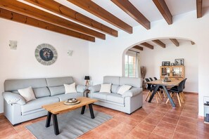 Een woonkamer met twee grijze banken, een houten salontafel en een eethoek met een houten tafel en stoelen.