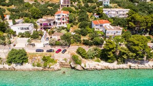 Vue aérienne d’une zone résidentielle côtière, avec des maisons, une mer turquoise aux eaux limpides et une côte rocheuse.
