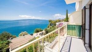 Un balcon avec vue sur la mer, un immeuble avec une porte verte et un ciel dégagé.