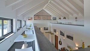 Un interior moderno con paredes blancas, techo inclinado y una larga zona de comedor con mesas y sillas.