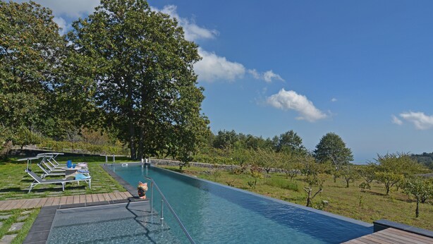 Una piscina infinita rectangular con agua azul cristalina, rodeada por una terraza de madera y sillas de descanso.