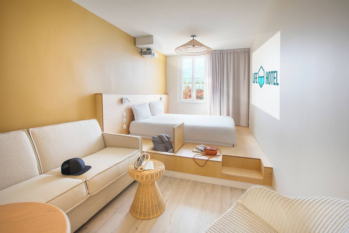 A hotel room with a bed, a sofa, a small table, and a window with curtains.