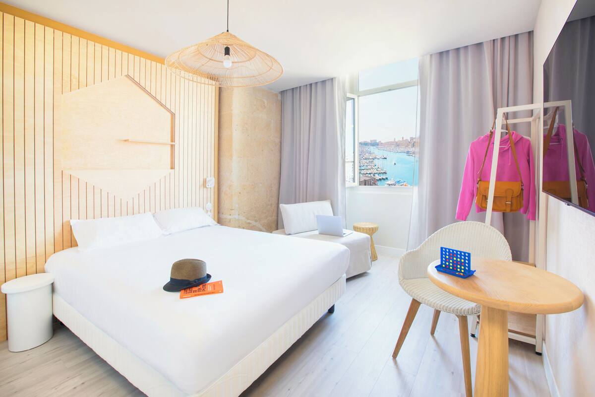 A hotel room with a large bed, a desk with a chair, a laptop, and a view of the sea.