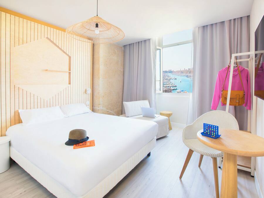 Quarto de hotel com uma cama grande, uma escrivaninha com cadeira, um laptop e vista para o mar.