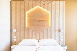 Une chambre d’hôtel moderne avec une tête de lit en bois, une table de chevet avec une lampe et un lit parfaitement fait.