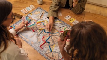 Un groupe de personnes joue à un jeu de société sur une table en bois, en utilisant un plateau de jeu représentant une carte et des pions.