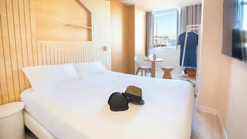 Habitación de hotel con cama, una mesita, una silla, televisor y vistas a la ciudad.