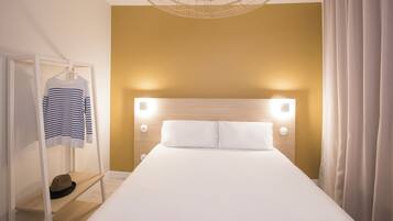 A hotel room with a bed, a hanging wardrobe, and a headboard with lights.