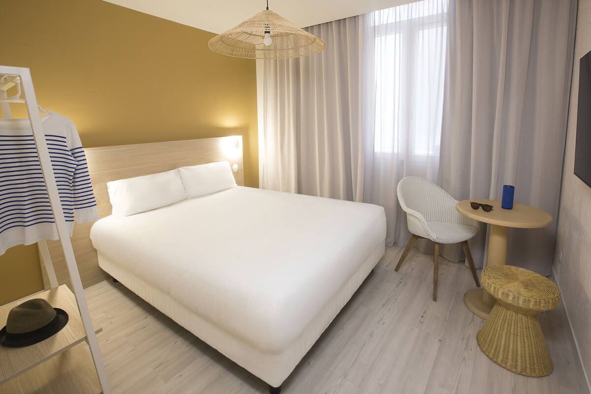 A hotel room with a large bed, a chair, a small table, and a hanging light fixture.