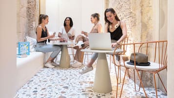 A group of people sitting around a table with a laptop, in a room with a terrazzo floor and exposed brick walls.