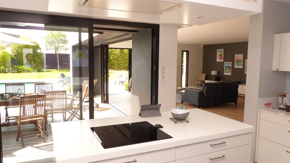 A modern kitchen with a large island, sliding glass doors leading to a patio, and a living area with a sofa and table.