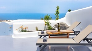 Une terrasse ensoleillée avec vue sur la mer, comprenant une table en bois avec une bouteille et des verres, des chaises longues et des plantes en pot.