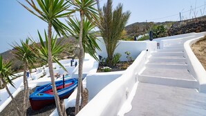 Un bâtiment aux murs blancs, avec un escalier menant à une zone abritant une piscine, le tout entouré de palmiers et d'un bateau bleu.