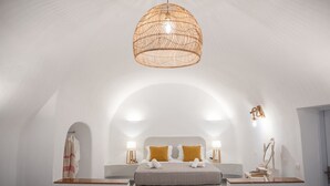 Une chambre moderne avec un grand lit, deux tables de chevet avec des lampes, un luminaire suspendu et une porte en arc blanc.
