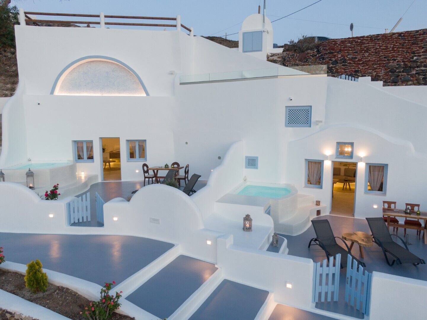 Un edificio blanco con piscina, sillas de descanso y una mesa.