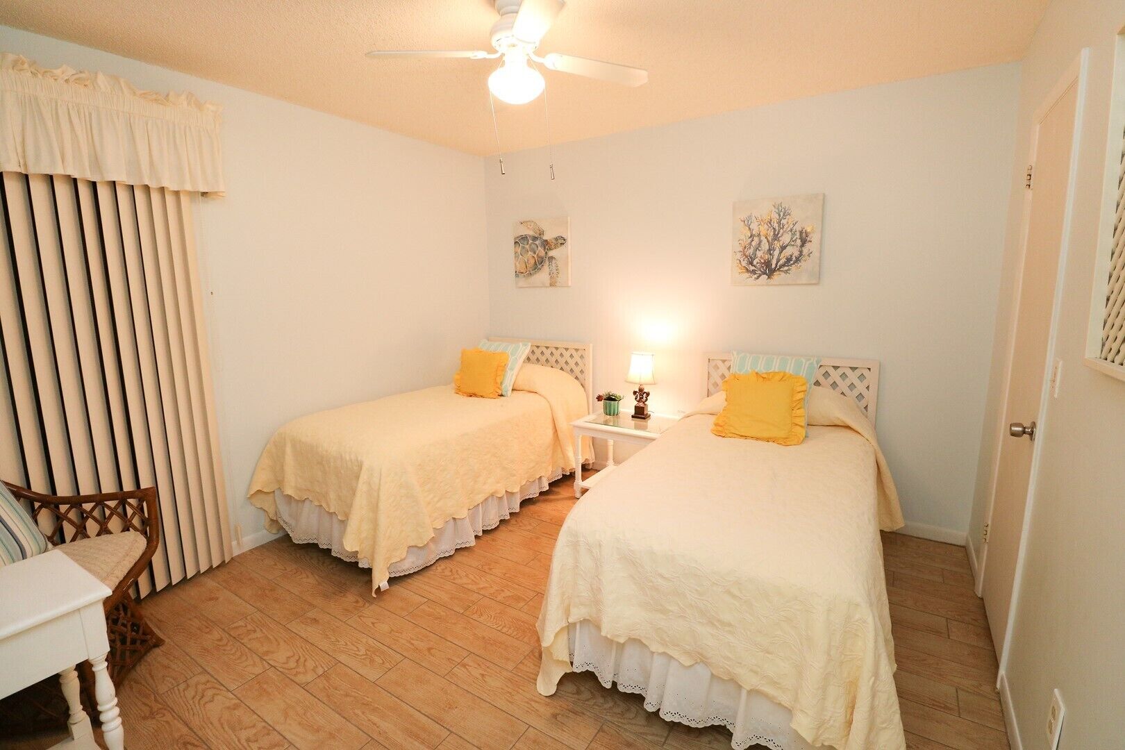 Une chambre avec deux lits, un ventilateur de plafond, une petite table avec une lampe et une chaise.