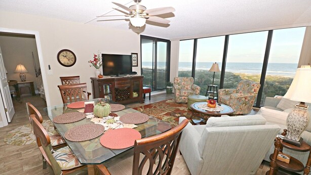 A spacious living room with a large dining table, comfortable seating, a television, and a view of the ocean. - Anastasia Condos 409- Luxury Direct Oceanfront Fourth Floor Condo (St Augustine)