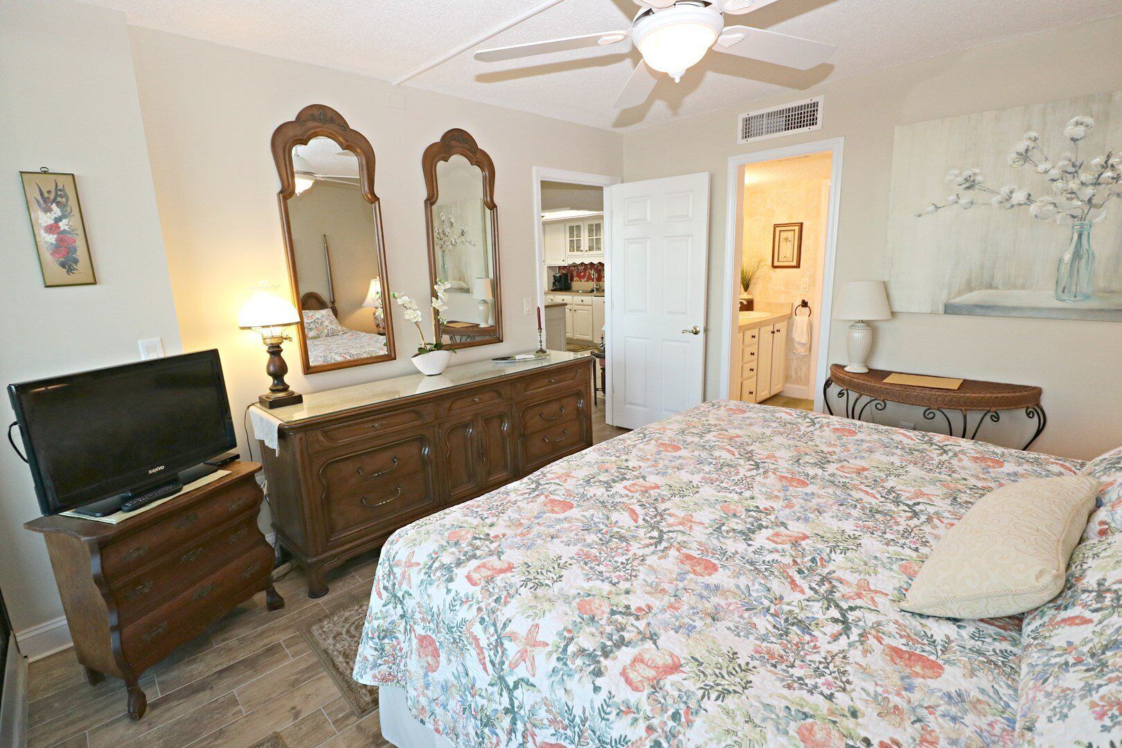 A bedroom with a bed, dresser, television, and a ceiling fan.