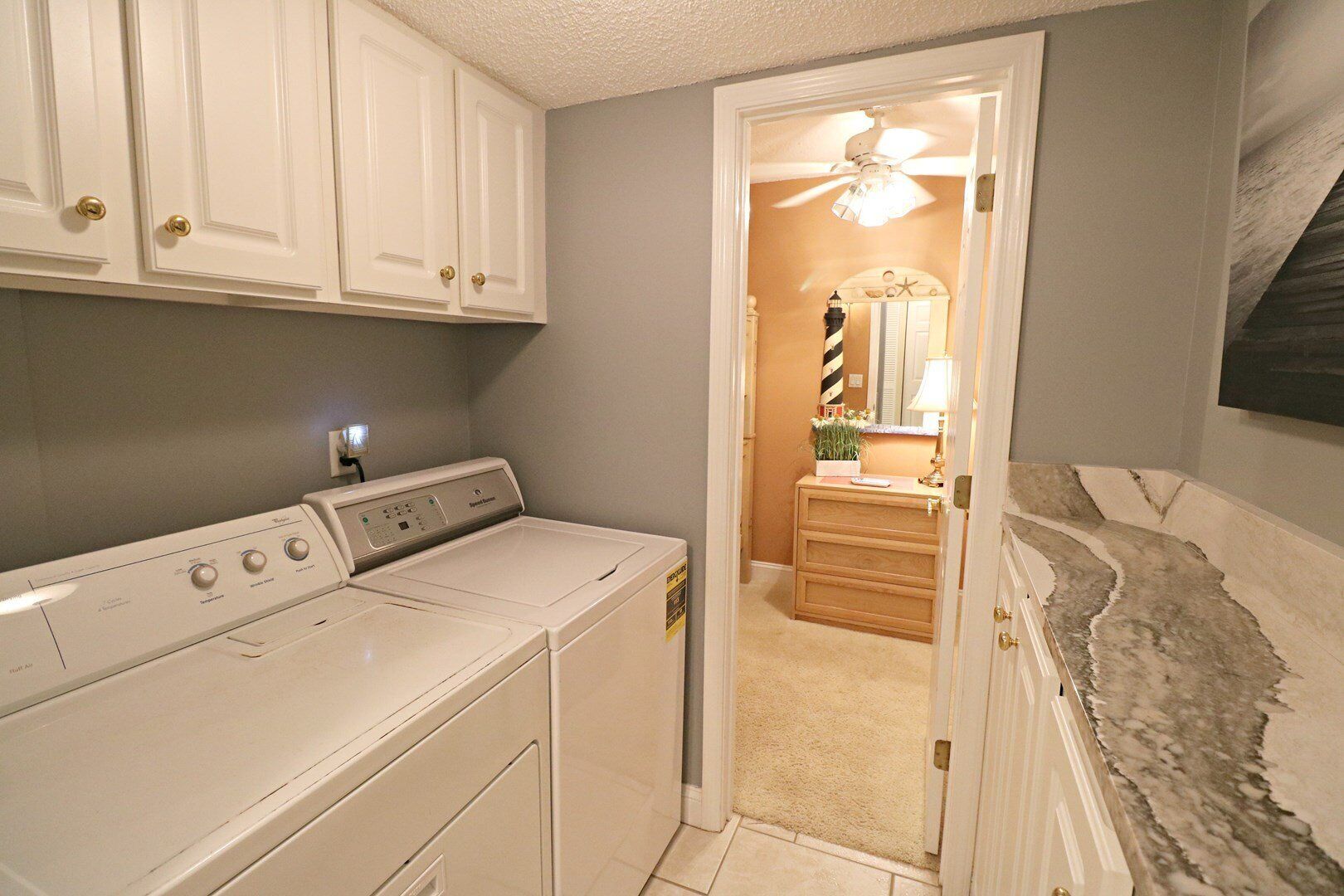 A laundry room with a front-loading washer and dryer, a ceiling fan, and a vanity with a mirror and countertop.
