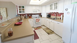 A kitchen with white cabinets, a microwave, an oven, a sink, and a refrigerator. - Anastasia Condos 409- Luxury Direct Oceanfront Fourth Floor Condo (St Augustine)