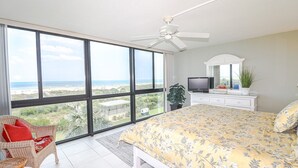 A bedroom with a large window, a bed, a television, and a ceiling fan.