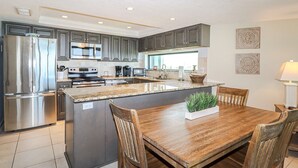 A modern kitchen with dark cabinets, stainless steel appliances, a granite countertop, and a wooden dining table with chairs.