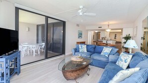 Een moderne woonkamer met een blauwe bank, een glazen salontafel en een tv op een meubel.