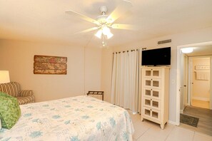 Ein Schlafzimmer mit einem Bett, einem Deckenventilator, einem Fernseher auf einer Kommode und einer Tür zu einem Badezimmer.
