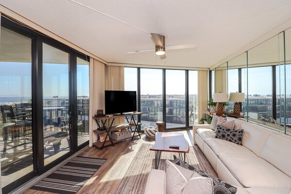 A spacious living room with a large flat-screen TV, a ceiling fan, and a sofa with decorative pillows.