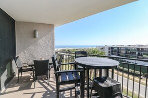 Un balcone con tavolo e sedie, vista sull'oceano e un edificio sullo sfondo.