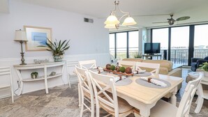 Een eetruimte met een houten tafel, witte stoelen en een kroonluchter. Er is een televisie en een balkon met uitzicht.