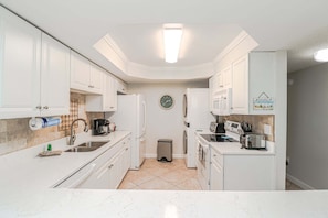 A compact kitchen with white cabinetry, a sink, a clock, and a trash bin.